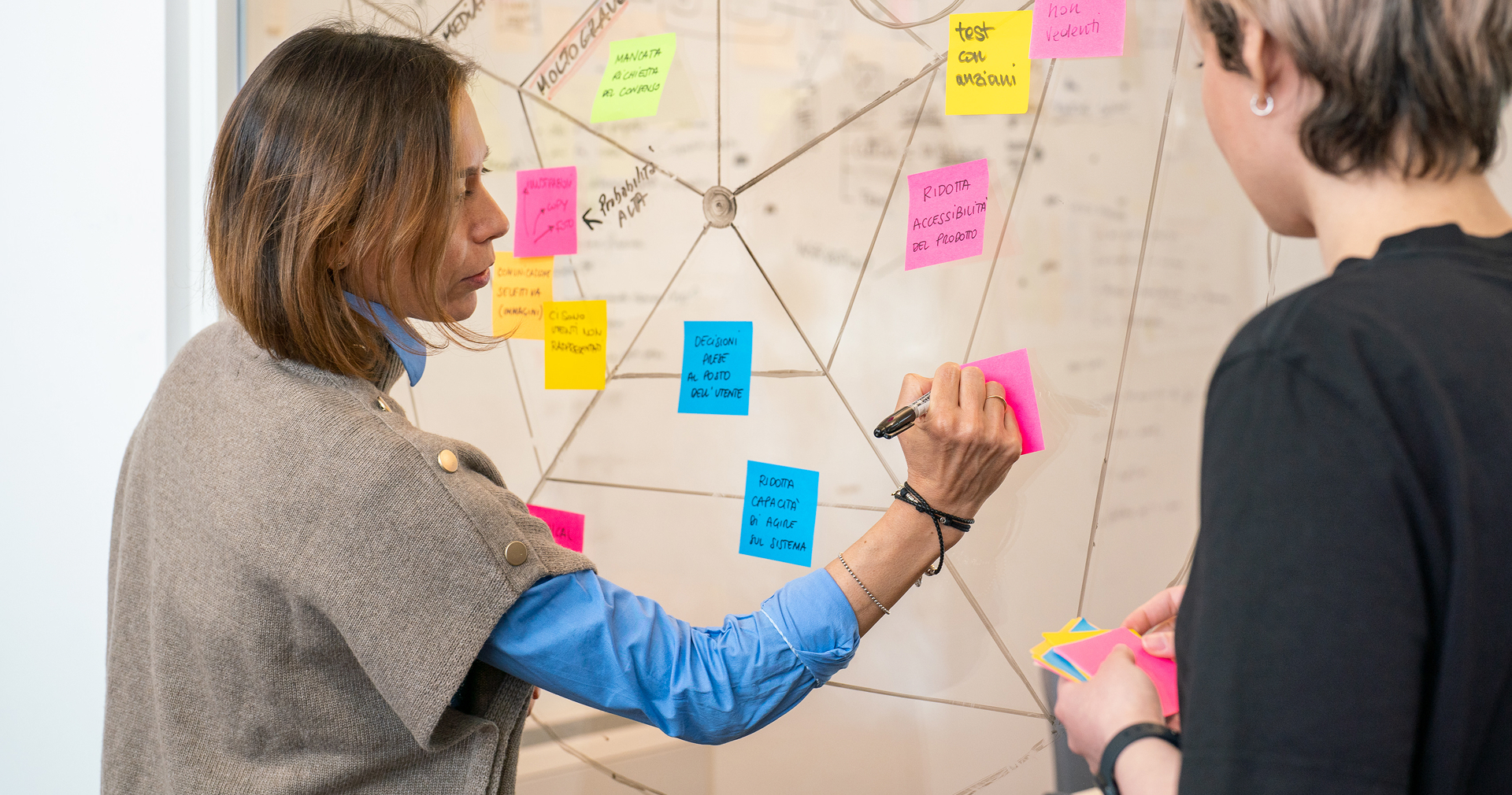 Two people write on coloured Post-It notes during a UX co-design session.