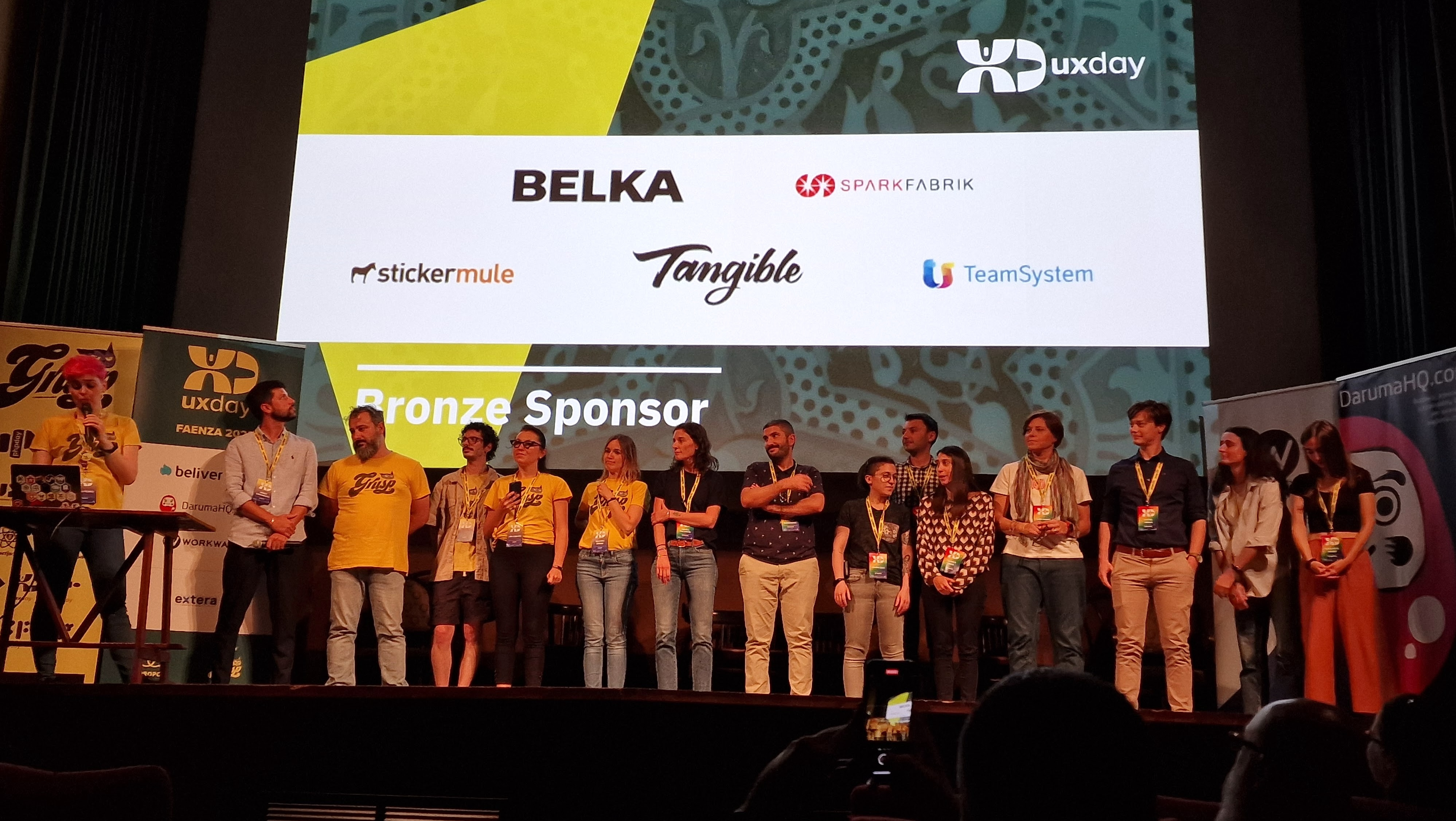 Gli speaker di uxday 2023 sul palco del Cinema Teatro Sarti di Faenza. Sullo sfondo una slide con alcuni degli sponsor dell'evento.